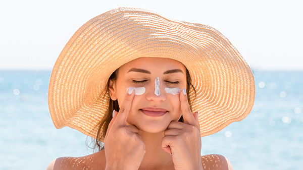 Mujer en la playa con sombrero y crema en la cara